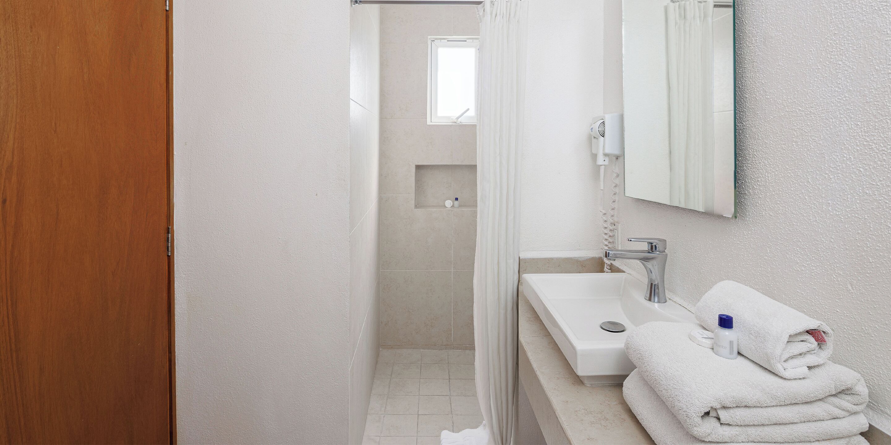 A bathroom with a wooden door, a white sink, a mirror, and a towel stack.