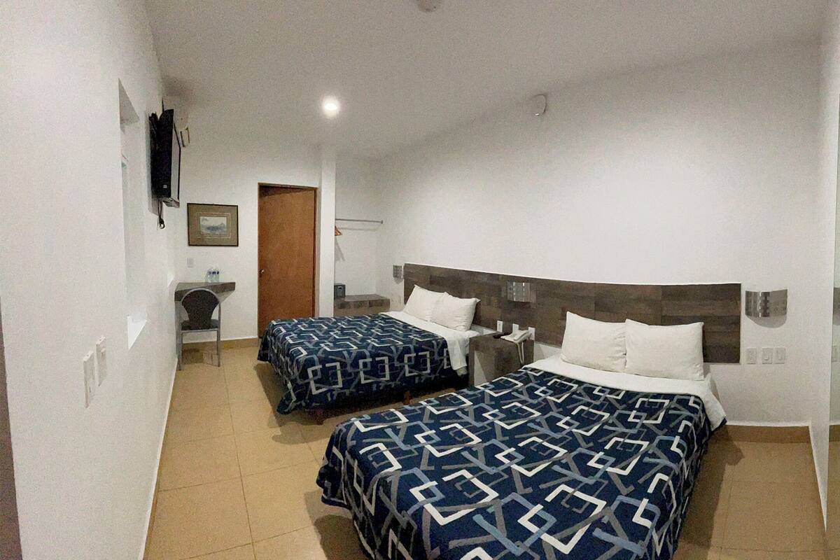 A hotel room with two beds, a TV, and a door leading to another room.
