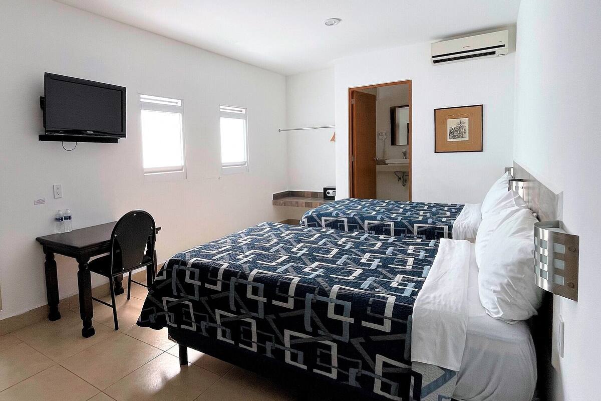A hotel room with a bed, a desk, a chair, a TV, and a bathroom visible through an open door.
