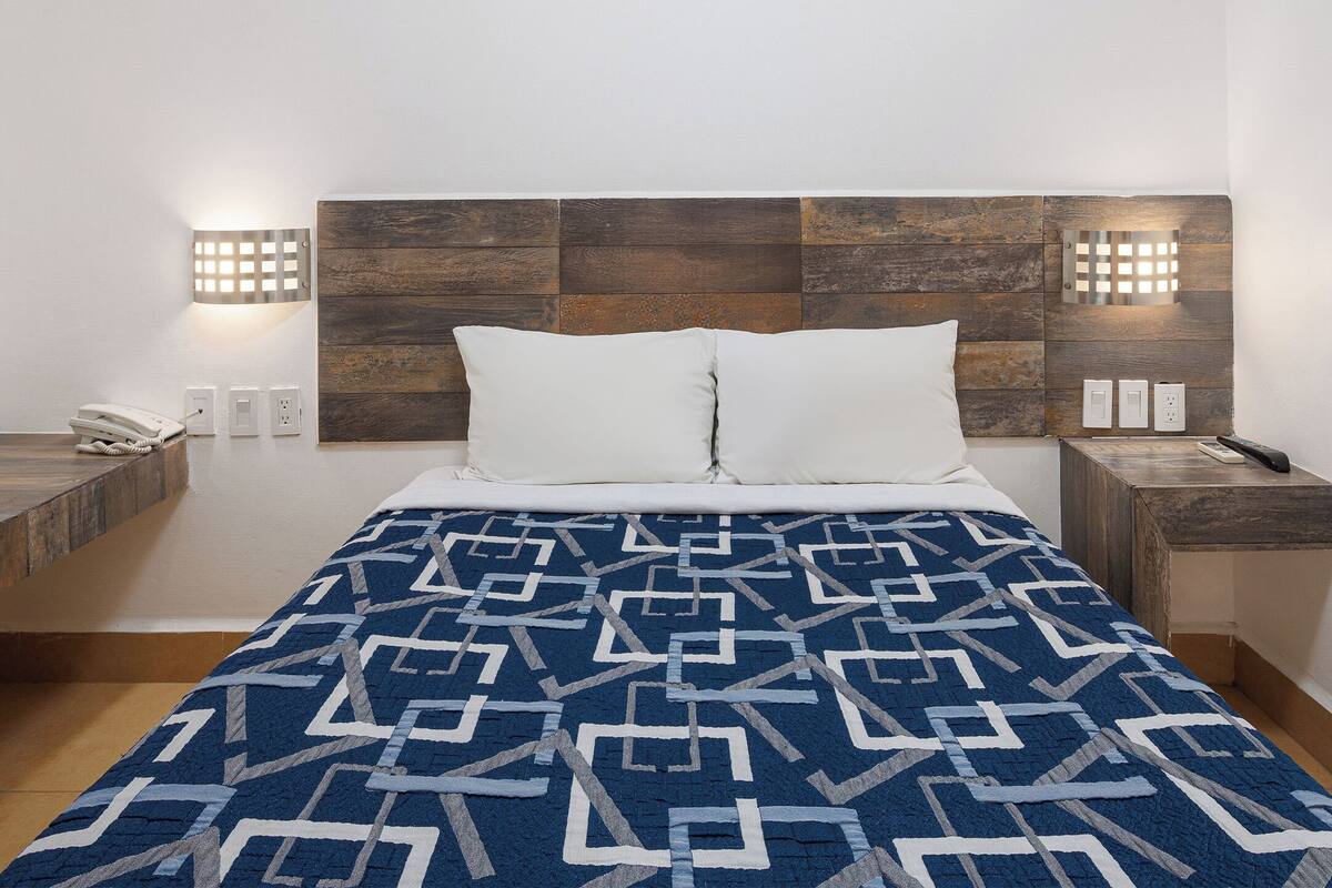 A bedroom with a patterned bedspread, a wooden headboard, bedside lamps, and a telephone on the nightstand.