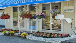 A building with a blue striped awning, a 'VACANCY' sign, and flower planters in front. - Friendship Oceanfront Suites (Old Orchard Beach)
