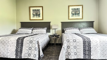 Habitación de hotel con dos camas, cada una con una colcha estampada, una mesita de noche con lámpara y dos cuadros en la pared.