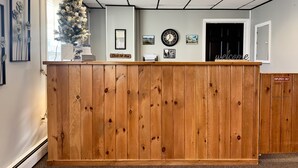 A reception desk with a wooden finish, a clock, framed pictures, and a 'Welcome' sign. - Colonial Valley Motel (Farmington)