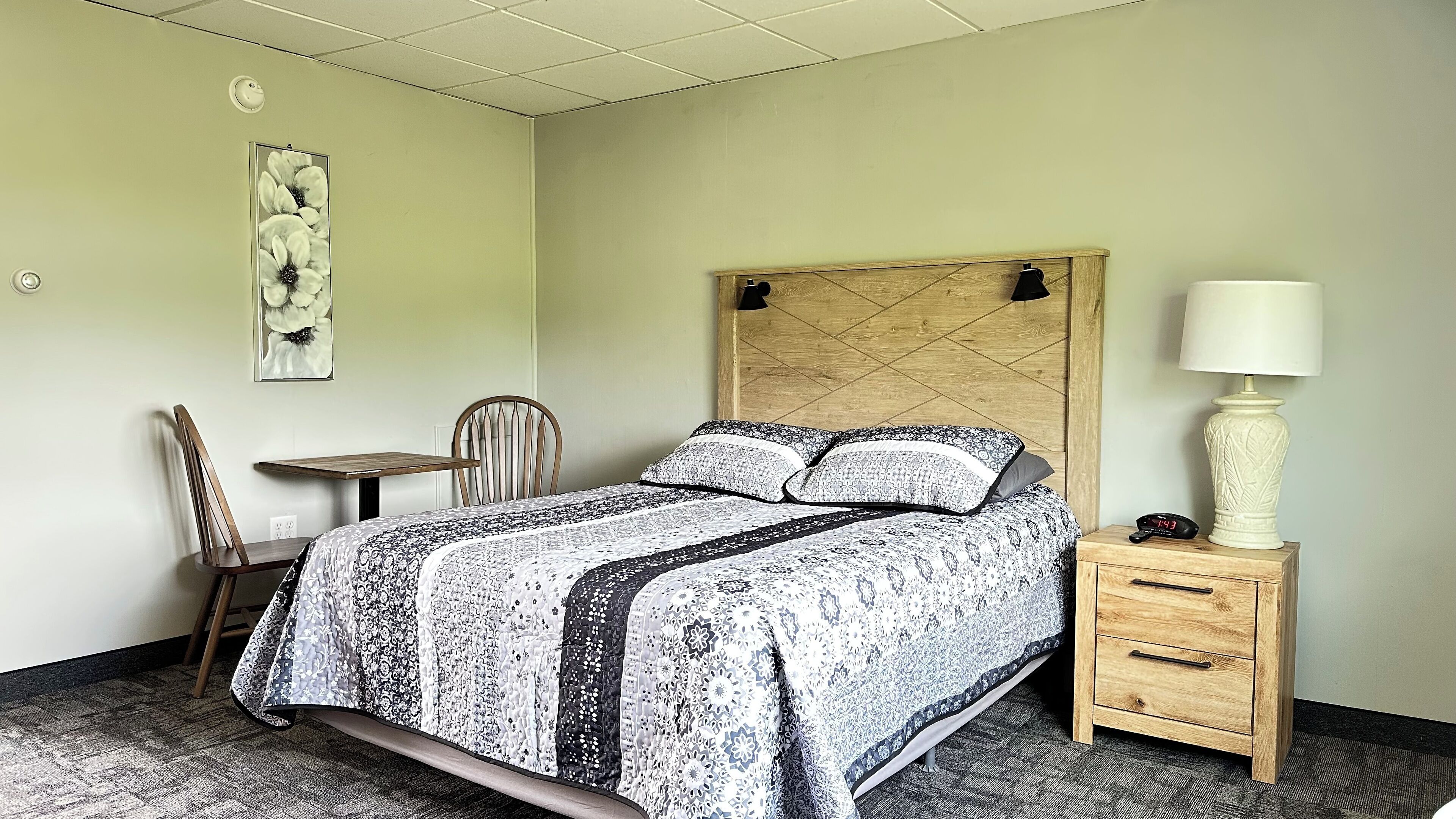 A bedroom with a bed, a chair, a table, a lamp, and a nightstand.