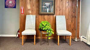 Two grey upholstered chairs with wooden legs, a small potted plant, a framed picture on the wall, and a floor lamp.