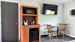A compact room with a kitchenette, including a microwave, coffee maker, and mini-fridge. There is a TV mounted on the wall and a small table with two chairs. - Colonial Valley Motel (Farmington)