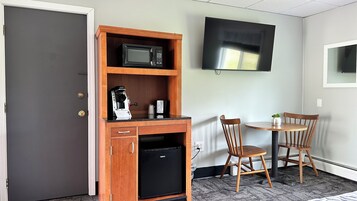 Habitación compacta con kitchenette, que incluye microondas, cafetera y refrigerador pequeño. Hay un televisor montado en la pared y una mesa pequeña con dos sillas.