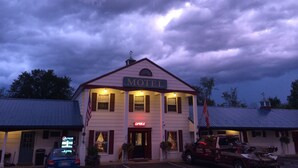 A motel with a central entrance, a flag, and a sign for a nearby office. - Colonial Valley Motel (Farmington)