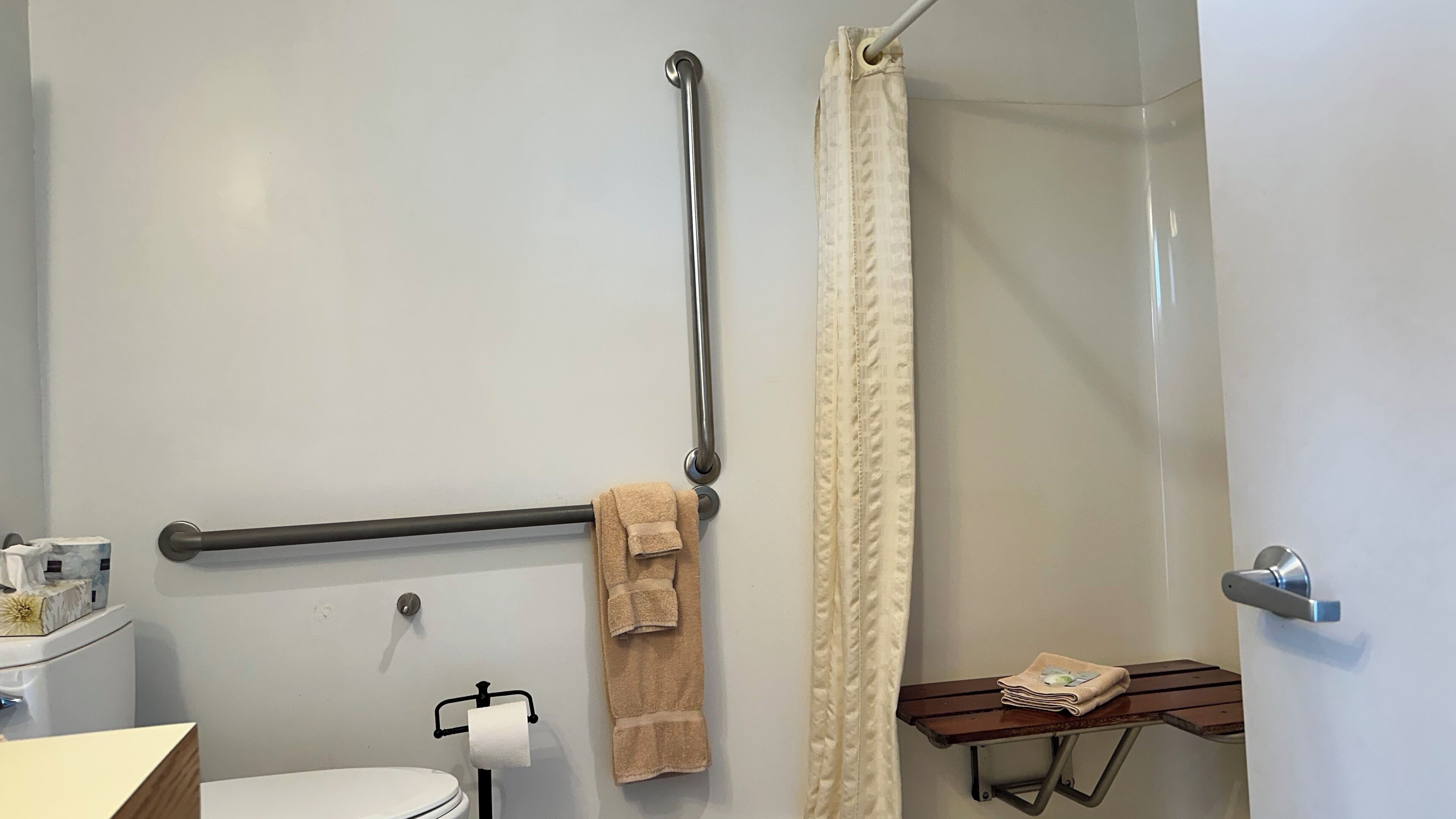 Bagno con il water, un corrimano, un porta asciugamani, una tenda per la doccia e un piccolo ripiano con asciugamani.