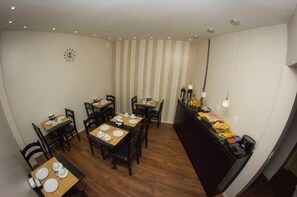 Un comedor con varias mesas y sillas, un mostrador de buffet con alimentos, y un reloj en la pared.