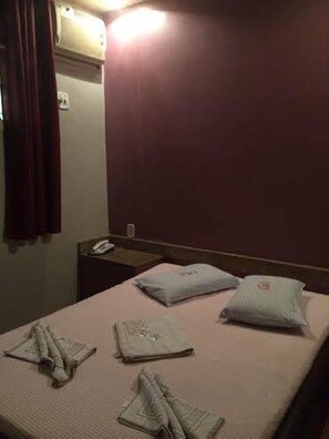 Een hotelkamer met een bed, nachtkastje, telefoon en een wandairconditioner.