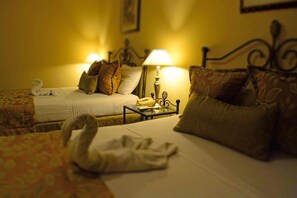 A hotel room with two beds, each with a swan-shaped pillow, a bedside table with a lamp, and a small table with a telephone. - Hotel Los Balcones Leon (León)