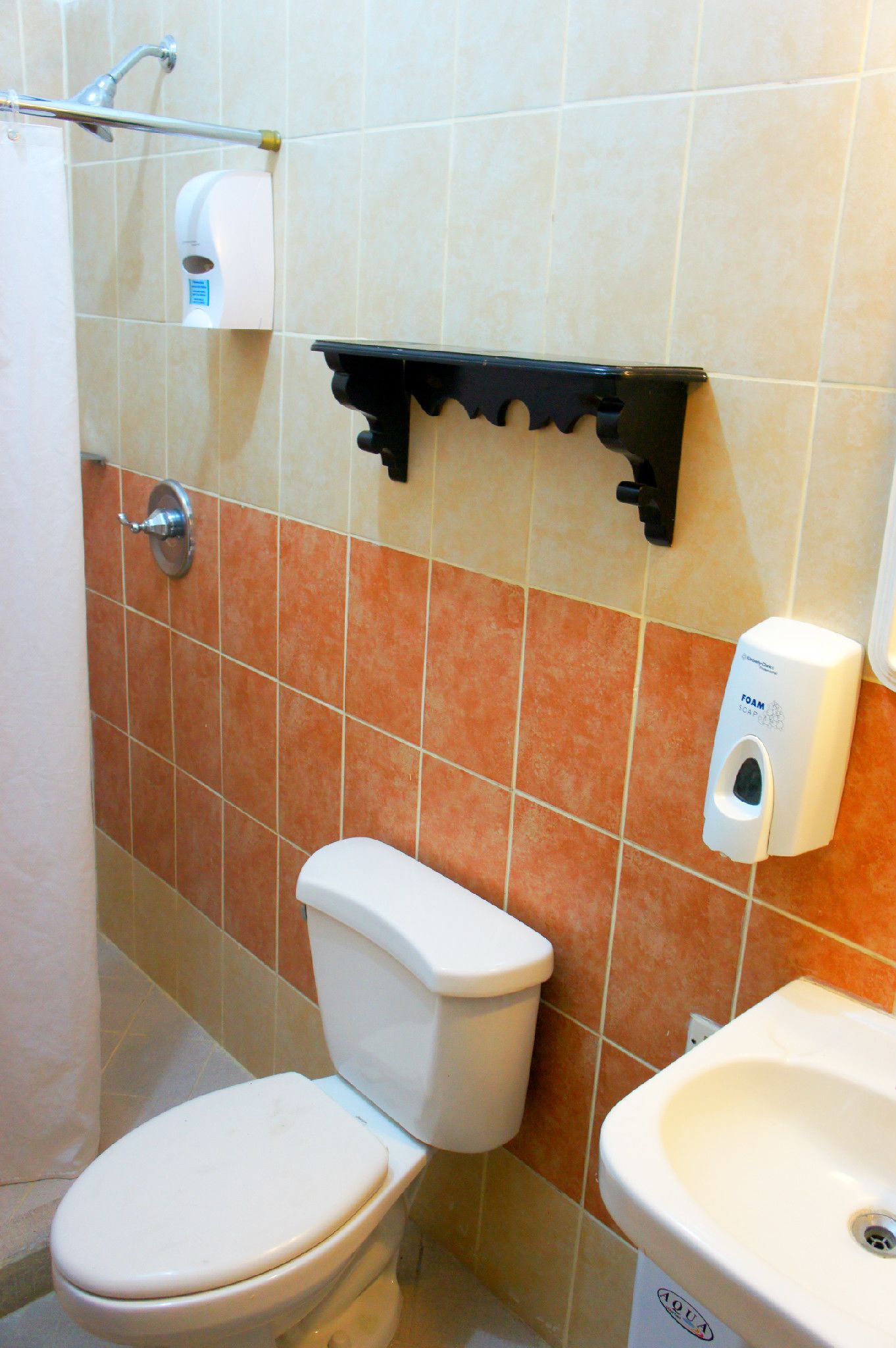 A bathroom with a toilet, sink, and a soap dispenser on the wall.