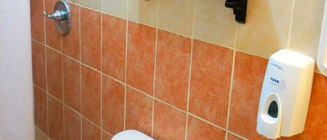 Un baño con inodoro, lavamanos y dispensador de jabón en la pared.