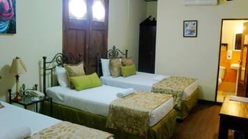 A hotel room with two single beds, a bedside table with a lamp, a wooden wardrobe, and a bathroom visible through an open door.