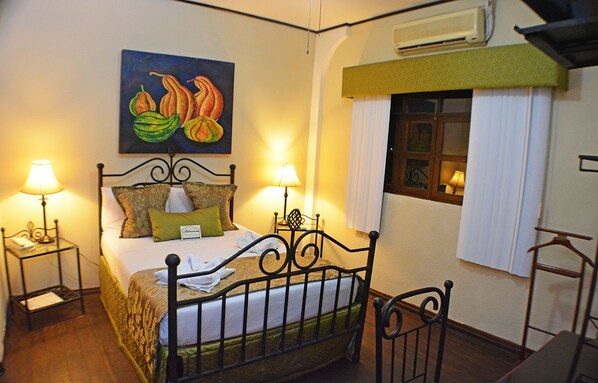 A neatly arranged bedroom with a bed, two bedside tables with lamps, a painting above the bed, and a window with curtains. - Hotel Los Balcones Leon (León)