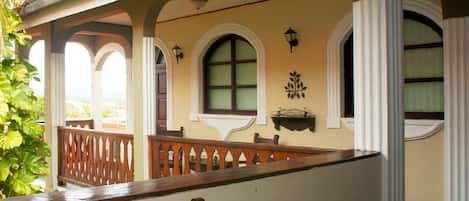 A covered balcony with wooden railings, a chair, and a wall-mounted shelf with decorative items.