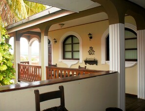A covered balcony with wooden railings, a chair, and a wall-mounted shelf with decorative items. - Hotel Los Balcones Leon (León)