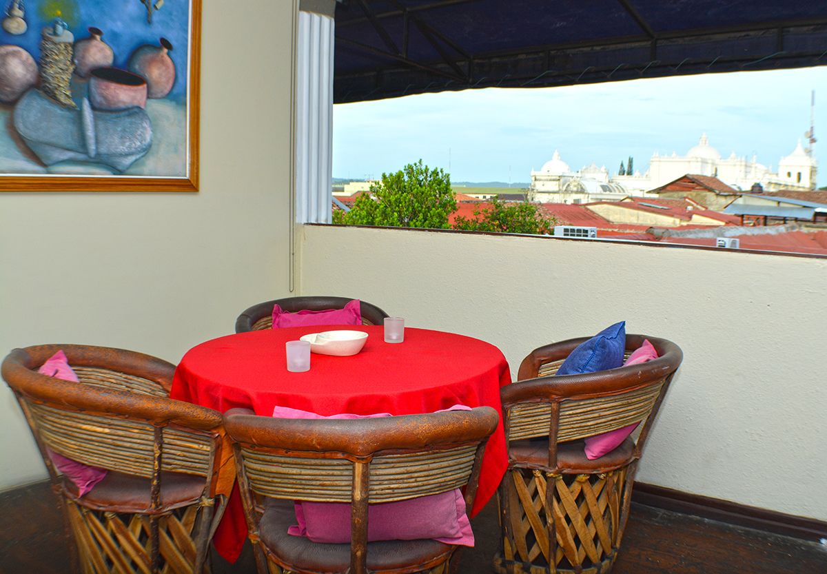 A dining area with a round table and wicker chairs, a red tablecloth, and a view of buildings in the background.