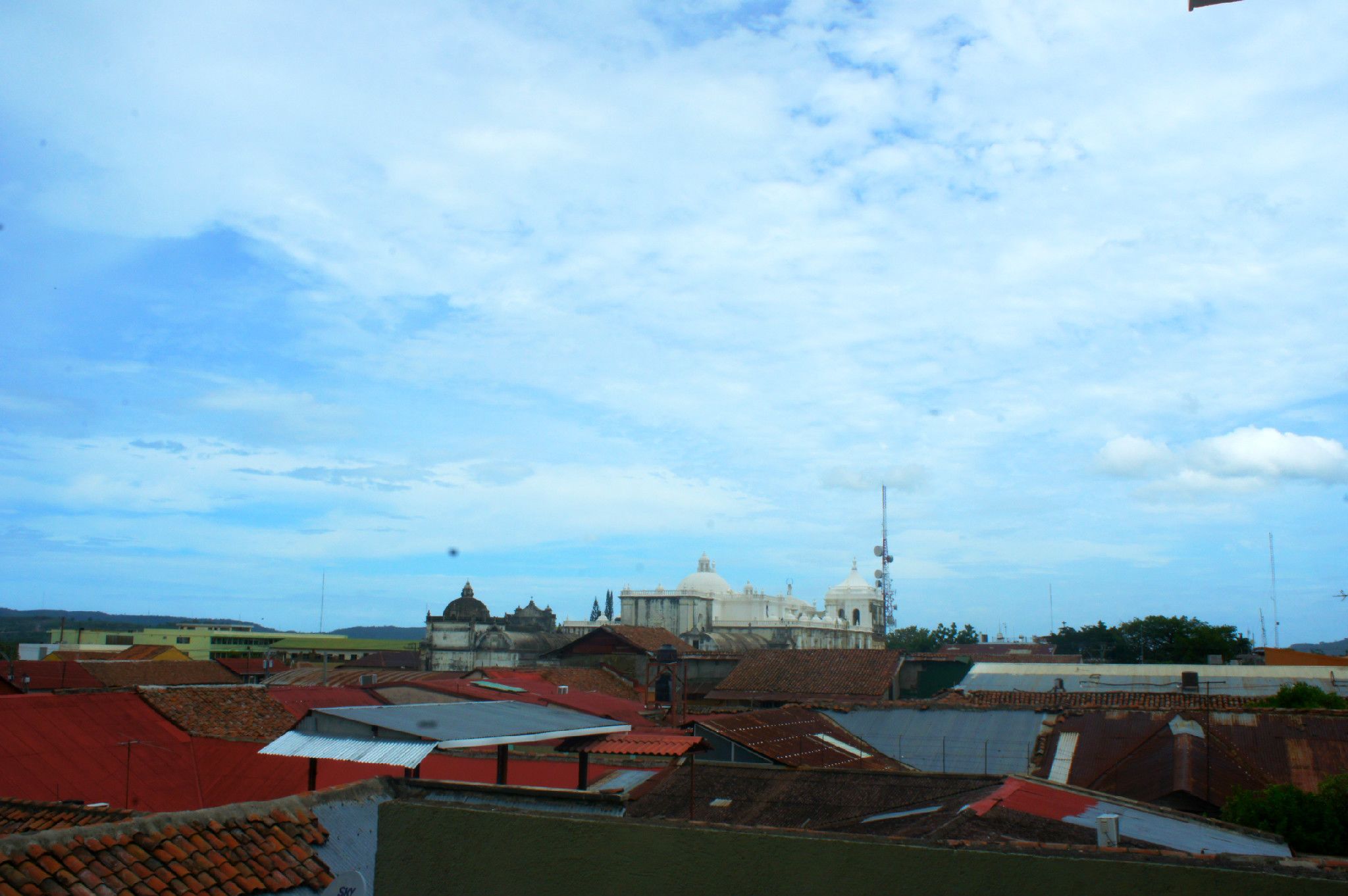 A view of a cityscape with a prominent white building with domes, surrounded by various buildings with red and yellow roofs.