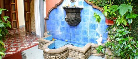 Un patio con una fuente, un muro de azulejos y plantas en macetas.