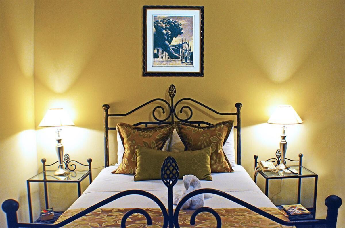 A neatly made bed with two lamps on either side, a framed picture above, and a small table with a phone and a magazine on the side.