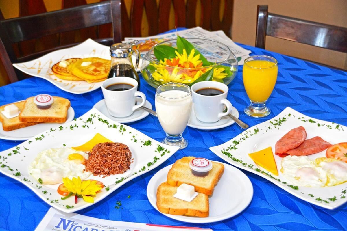 Une table de petit-déjeuner avec des assiettes remplies de nourriture, des tasses de café, un verre de jus d’orange et un journal.