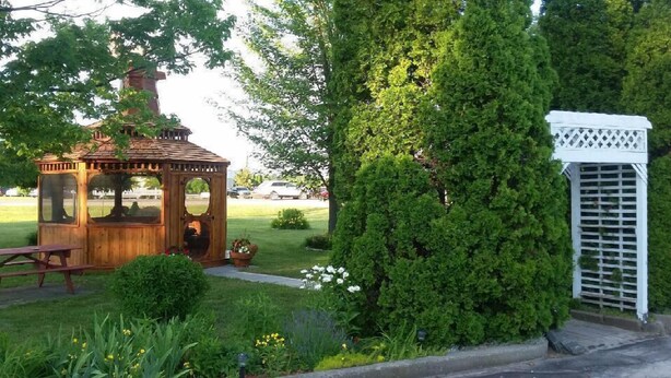 A wooden gazebo with a bench, surrounded by lush greenery and a white lattice structure.