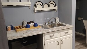 A compact kitchen with a sink, countertop, and white cabinets.