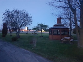 Un porche con chimenea, rodeado de árboles y una mesa de picnic.