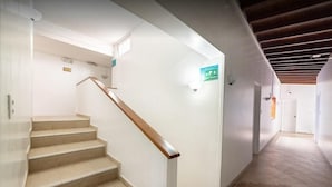 En trappe med lysegrå trin og trægelændere, der fører op til en platform med et grønt skilt for nødudgang.