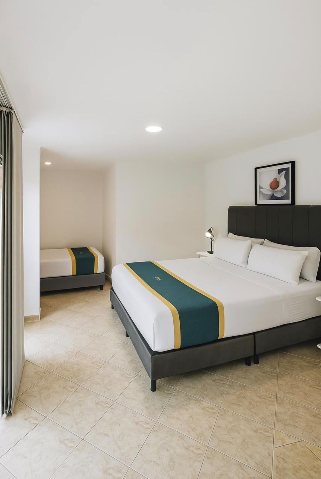 Una habitación de hotel con una cama grande, una cama más pequeña, una mesita de noche, una lámpara y un cuadro en la pared.