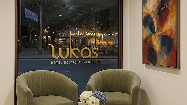 En hotellobby med to grønne lænestole, et træbord med en vase blomster, og et stort abstrakt maleri på væggen.
