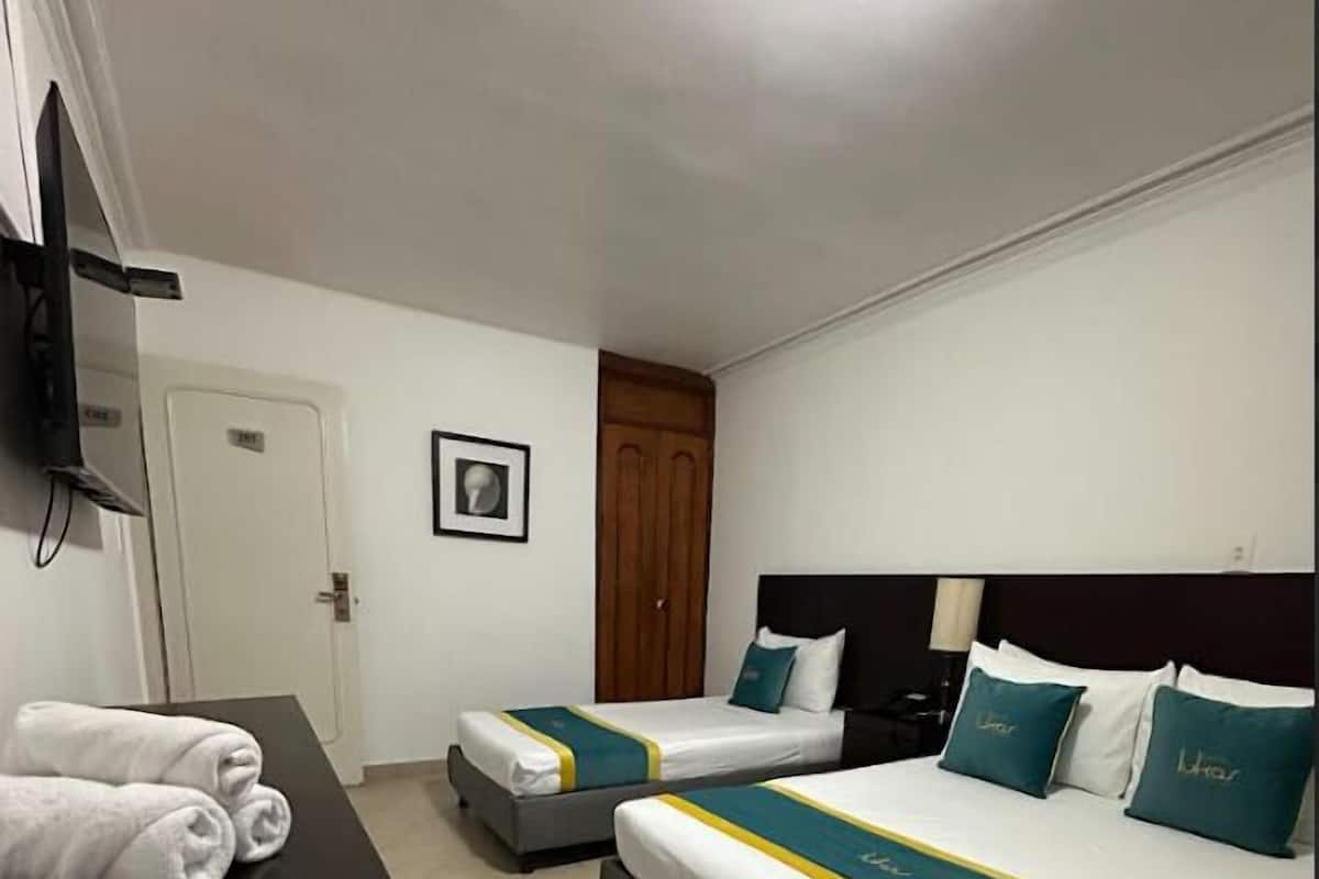 A hotel room with two beds, a flat-screen TV, a door, and a framed picture on the wall.