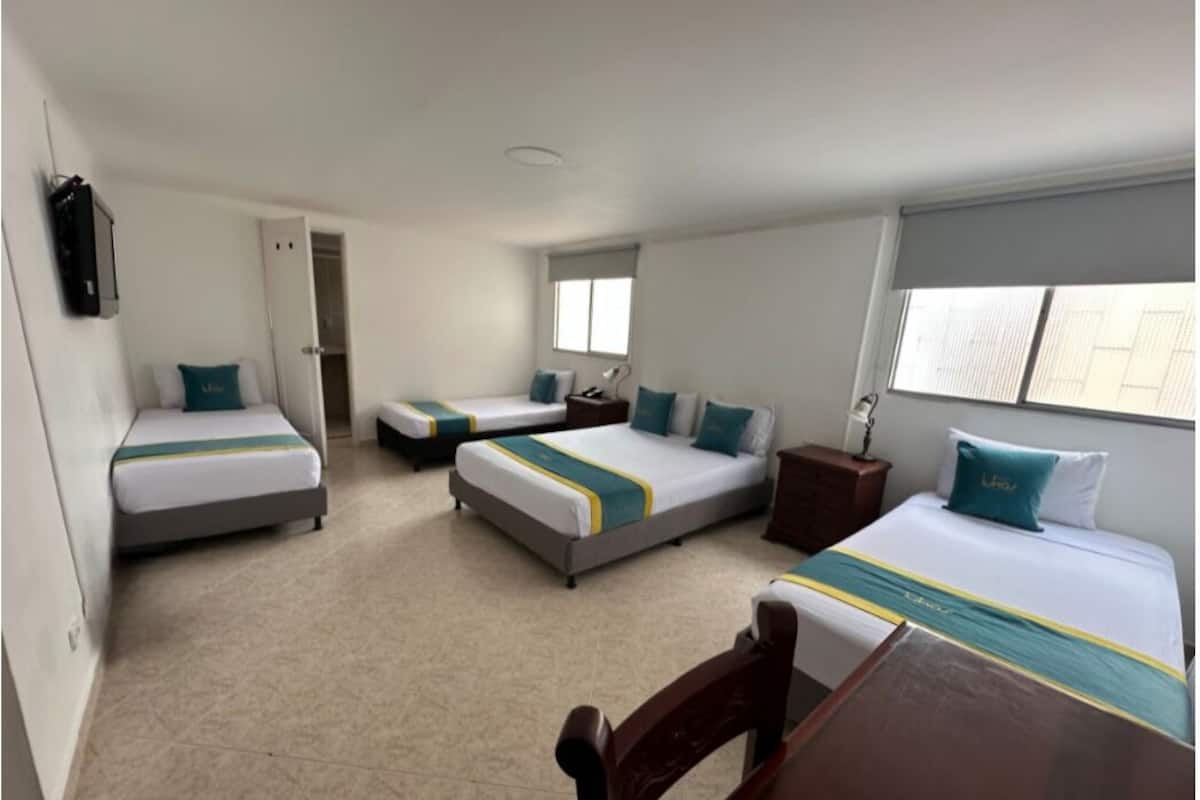 A hotel room with three beds, a wooden table, and a wardrobe.