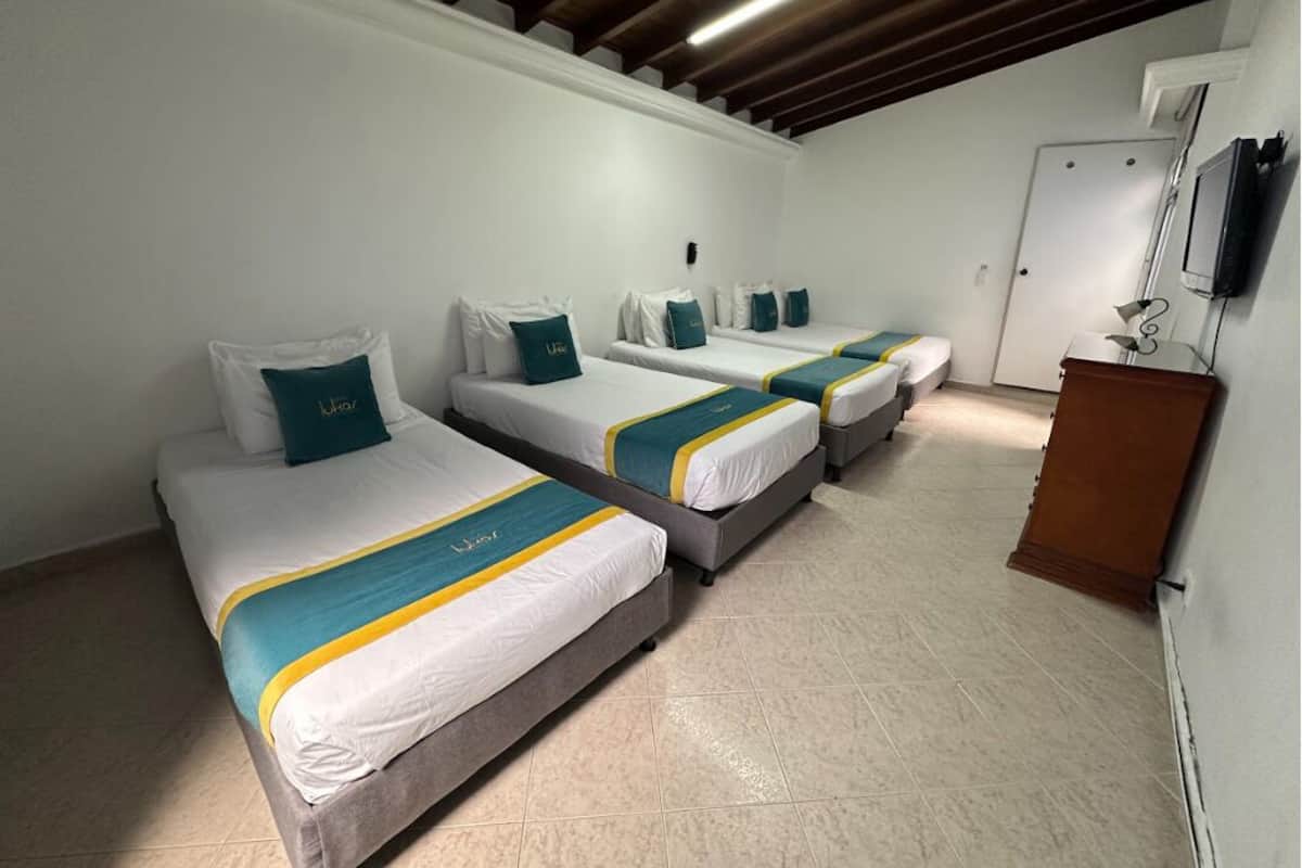 A hotel room with three beds, each with a white and teal bedspread, and a wooden ceiling.