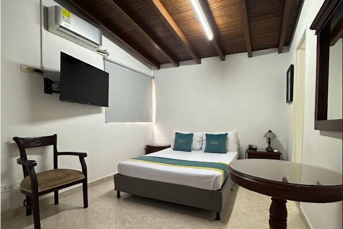 A bedroom with a bed, a chair, a table, and a TV mounted on the wall.