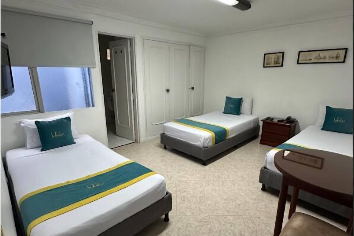 A hotel room with two beds, a desk, and a chair. There is a window with a view, a door, and a ceiling light.