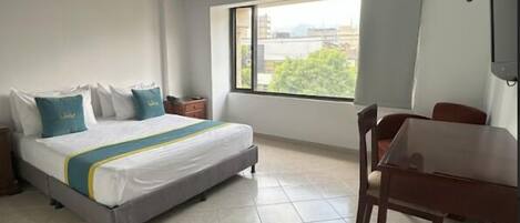 Un dormitorio con cama, ventana, mesa y silla.