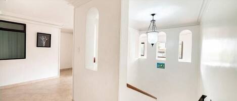A hallway with white walls, a tiled floor, and a staircase with a wooden handrail.