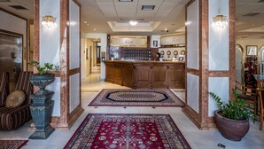 Eine Hotelhalle mit Empfangsschalter, Barbereich und einer Sitzecke mit gemustertem Teppich.