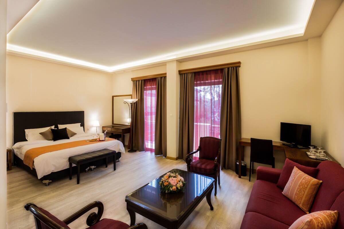 A hotel room with a bed, a desk, a television, a red armchair, a sofa, and a coffee table.
