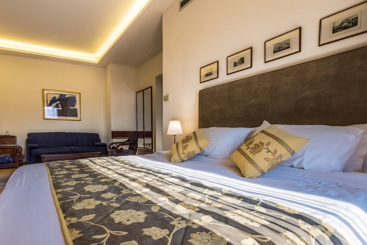 A hotel room with a large bed, a sofa, a lamp, and framed pictures on the wall.