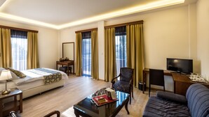 Ein Hotelzimmer mit Bett, Schreibtisch, Sessel, Sofa und Fernseher.