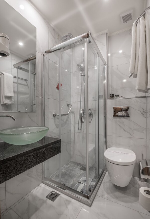 A modern bathroom with a glass-enclosed shower, a glass sink, and a white toilet.