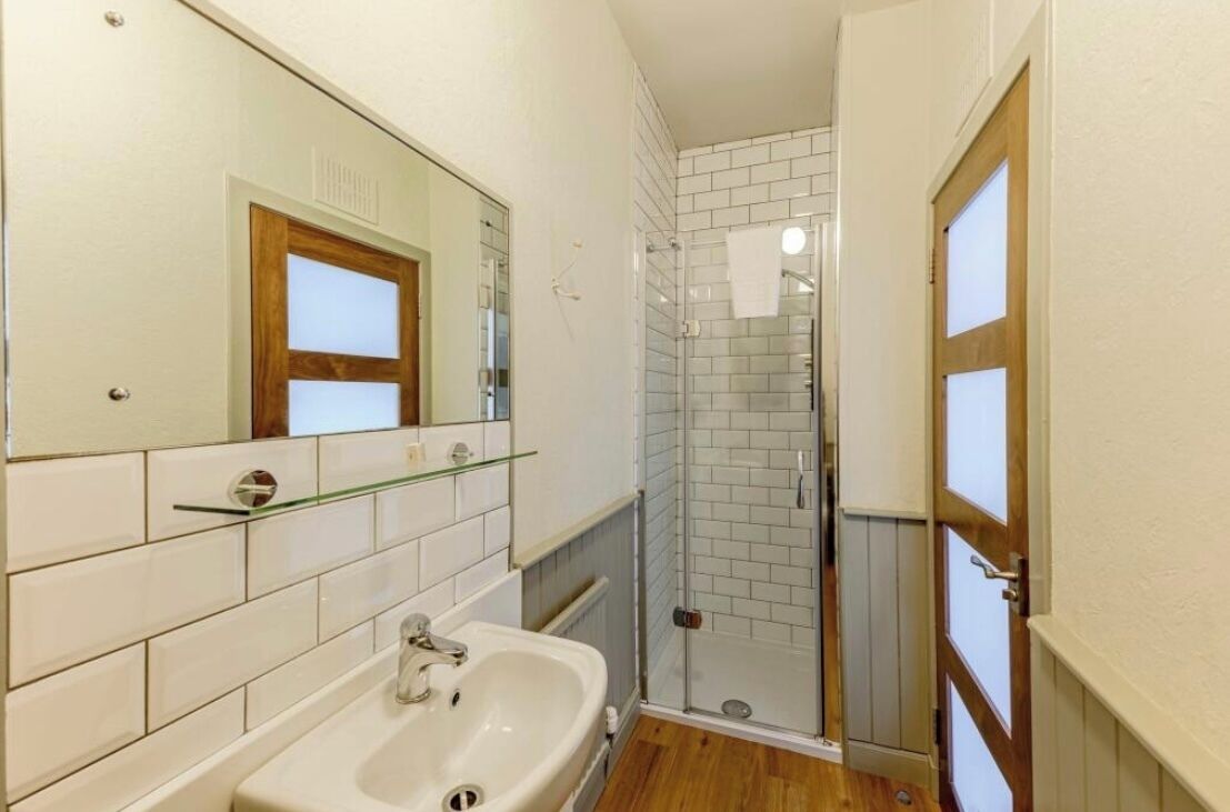 Une salle de bain avec un lavabo blanc, une cabine de douche en verre et une porte en bois.