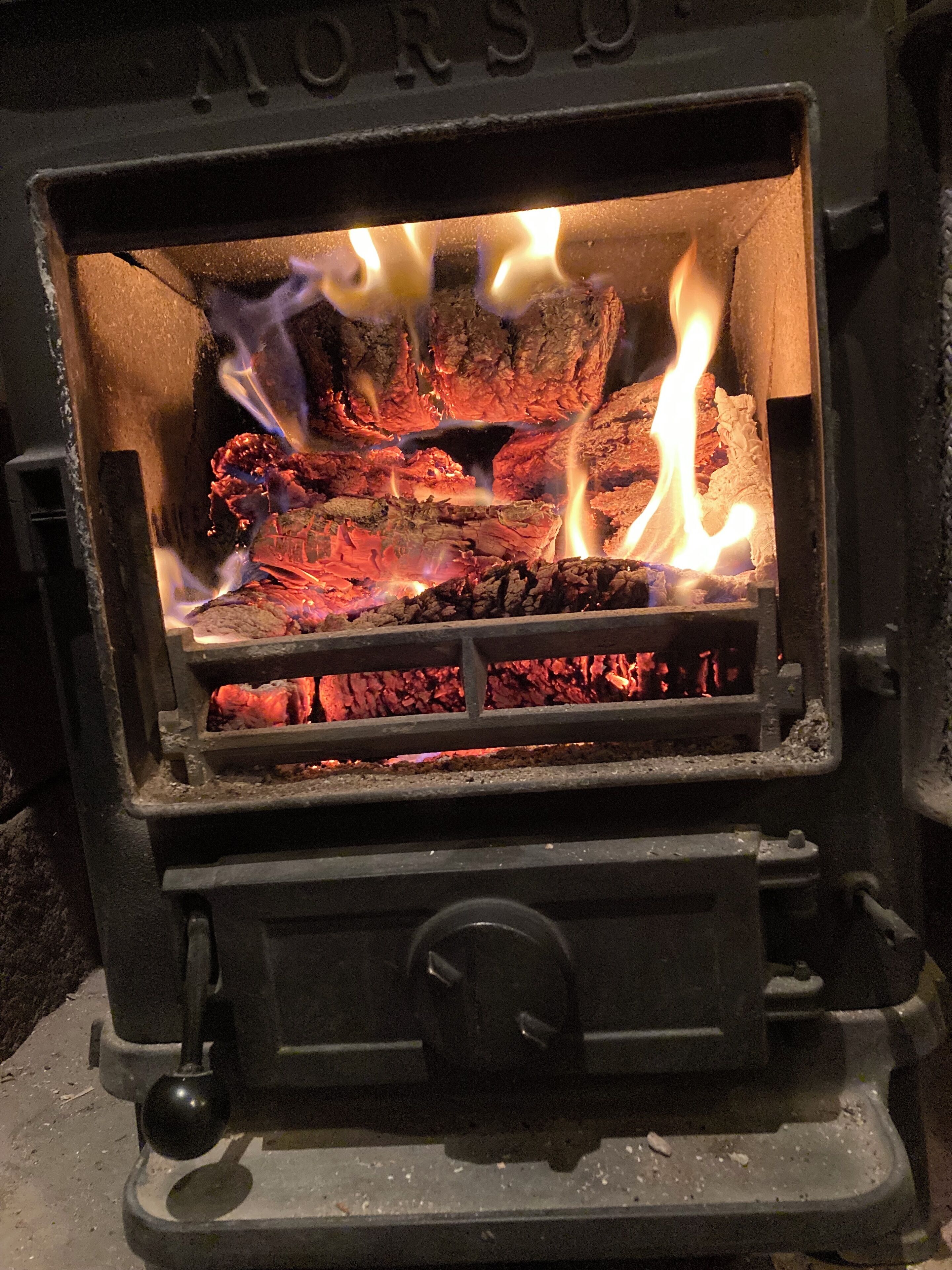 A wood-burning stove with visible flames and logs inside.