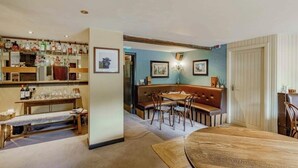 A cozy dining area with a wooden table and bench, a bar with shelves of bottles, and framed pictures on the walls. - Hightae B&B (Lockerbie)