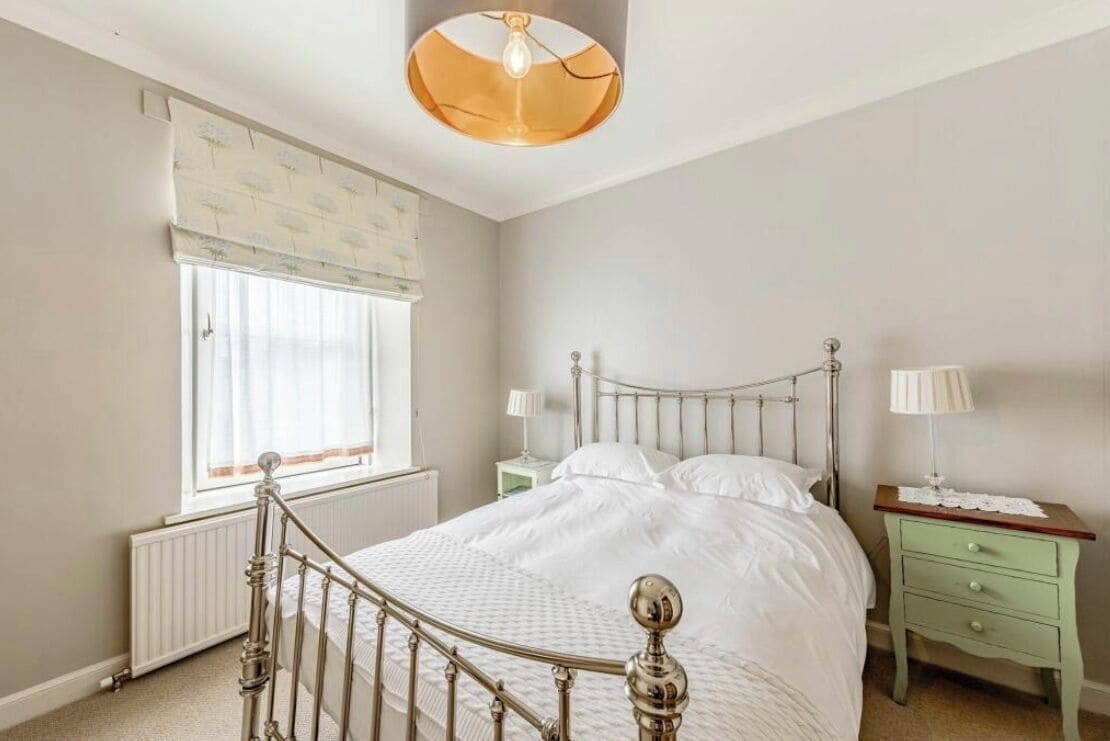 A bedroom with a bed, a nightstand, a lamp, a radiator, and a window with curtains.