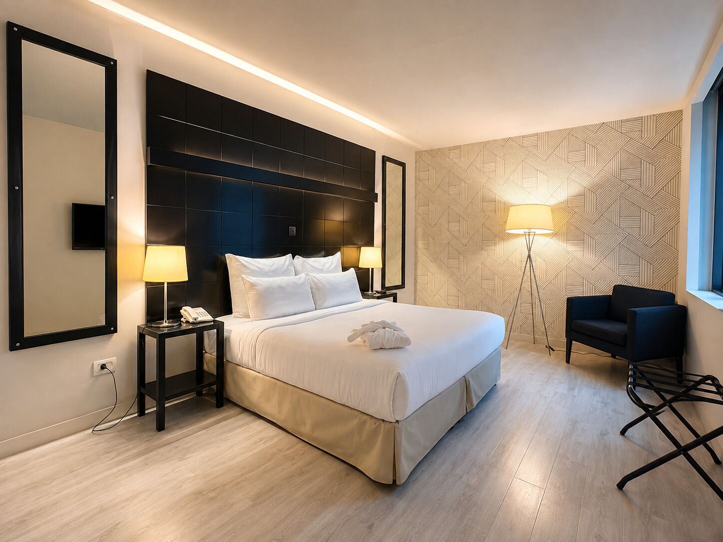 Habitación de hotel con una cama grande, lámparas de noche, un escritorio, una silla y una pared con diseño.